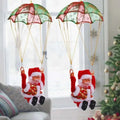 Two christmas-themed santa claus figurines suspended by green and pink climbing rainbow parachute toy with gold trim