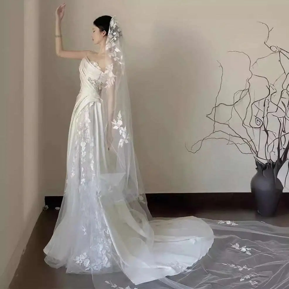 A flowing white lace wedding veil with floral appliqués and a sheer train paired with a satin lace wedding fishtail dress
