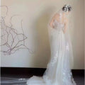 A flowing white satin lace wedding fishtail dress with delicate floral lace detailing and a matching lace wedding veil