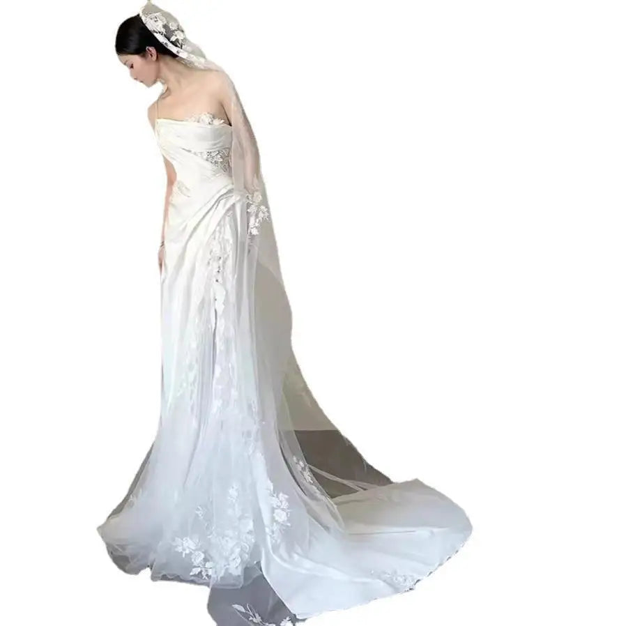 Back of a flowing white lace wedding veil with delicate floral embroidery paired with a satin lace wedding fishtail dress