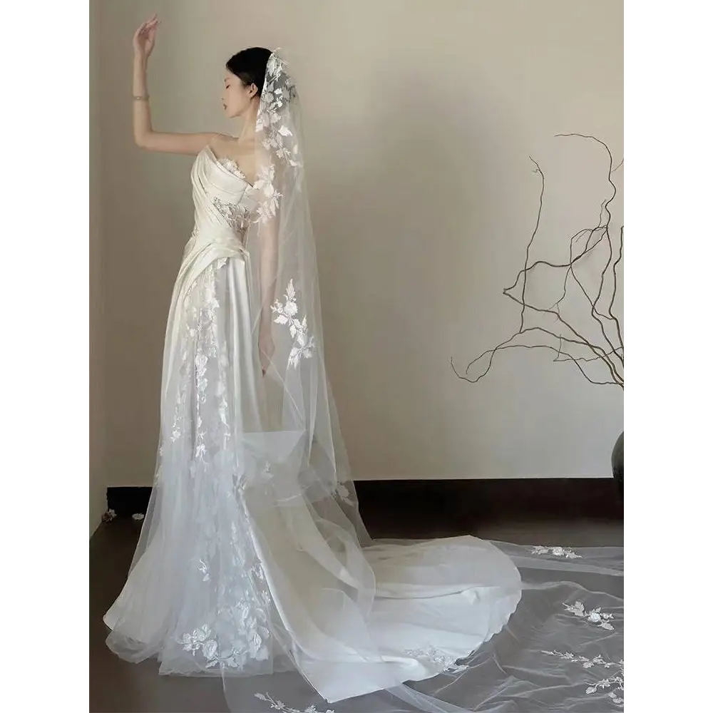 A flowing white satin lace wedding veil with delicate floral embroidery paired with a fishtail dress