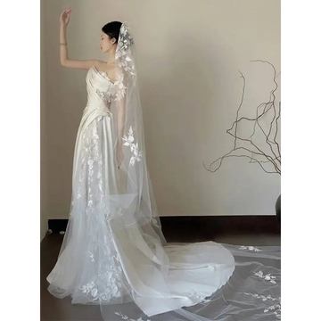 A flowing white satin lace wedding veil with delicate floral embroidery paired with a fishtail dress