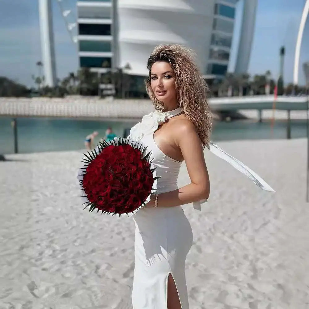 A lush bouquet of deep red roses with dark green thorns complements the satin white ribbon flower halter gown design