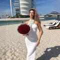 A woman in a satin white ribbon flower halter gown with an ornate floral neckline holding a bouquet of red roses