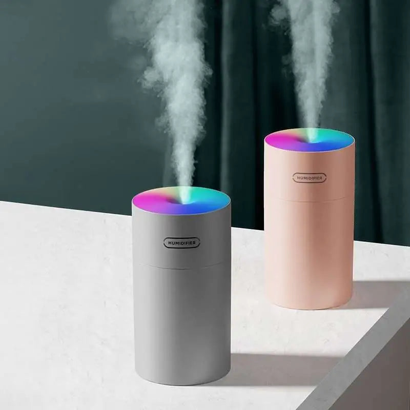 Two cylindrical colorful cup humidifiers usb in gray and peach with rainbow-lit tops emitting mist