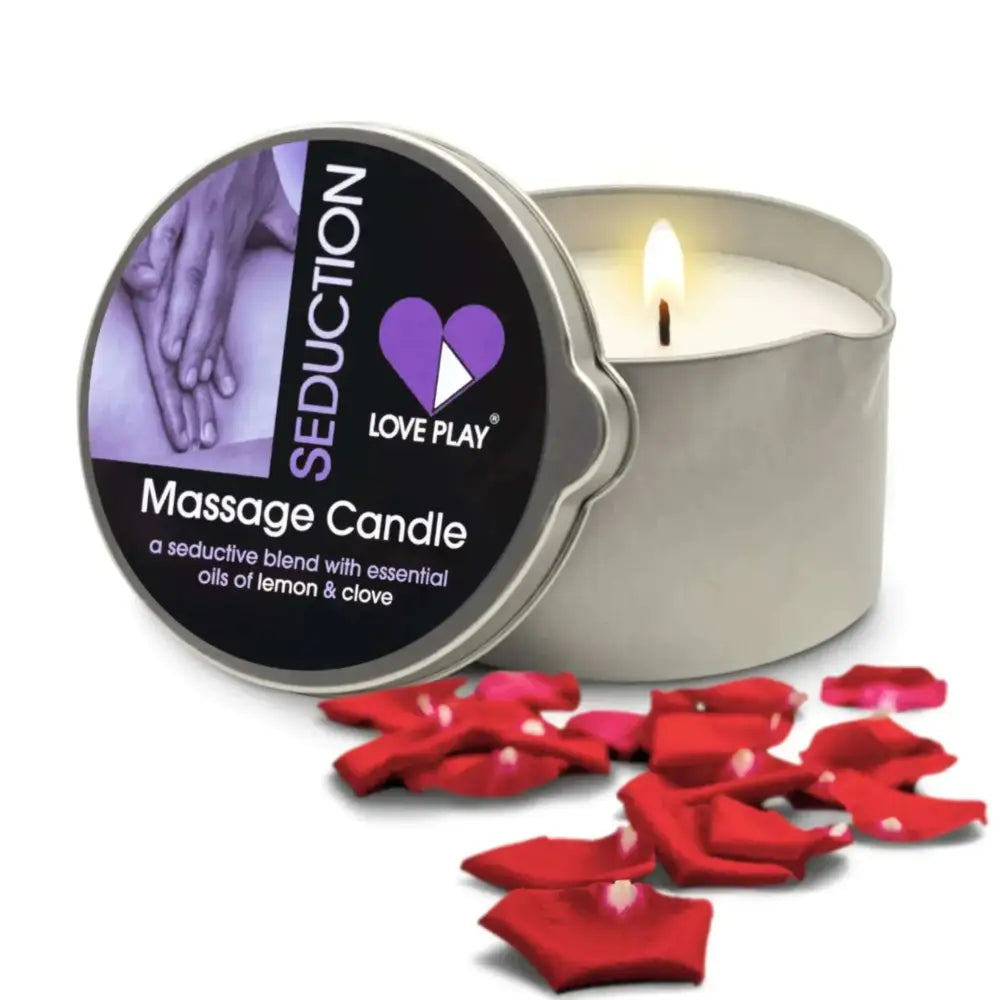 A lit silver tin massage oil candle labeled seduction massage oil by love play with lemon and clove essential oils