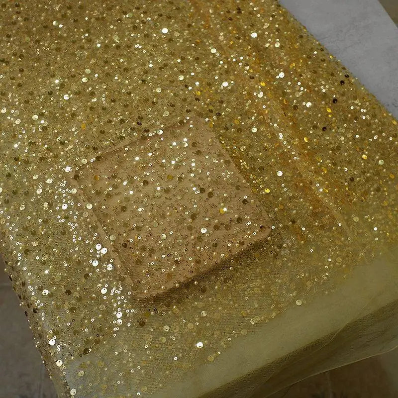 A translucent glass dish on dazzling gold sequined fabric complements the pearl embroidery lace asymmetric dress design