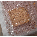 A square rose gold dazzling gold sequined makeup palette resting on sheer fabric complements pearl embroidery lace asymmetric dress