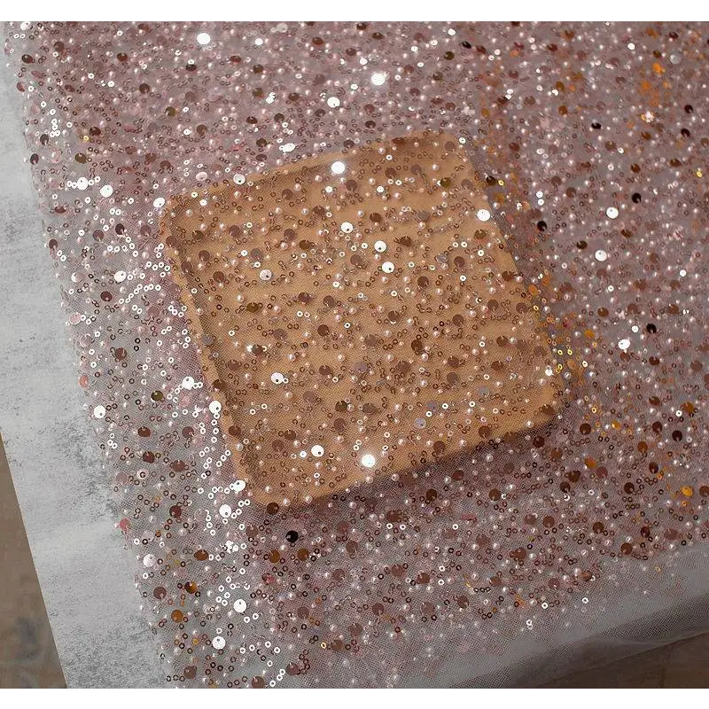 A square rose gold dazzling gold sequined makeup palette resting on sheer fabric complements pearl embroidery lace asymmetric dress