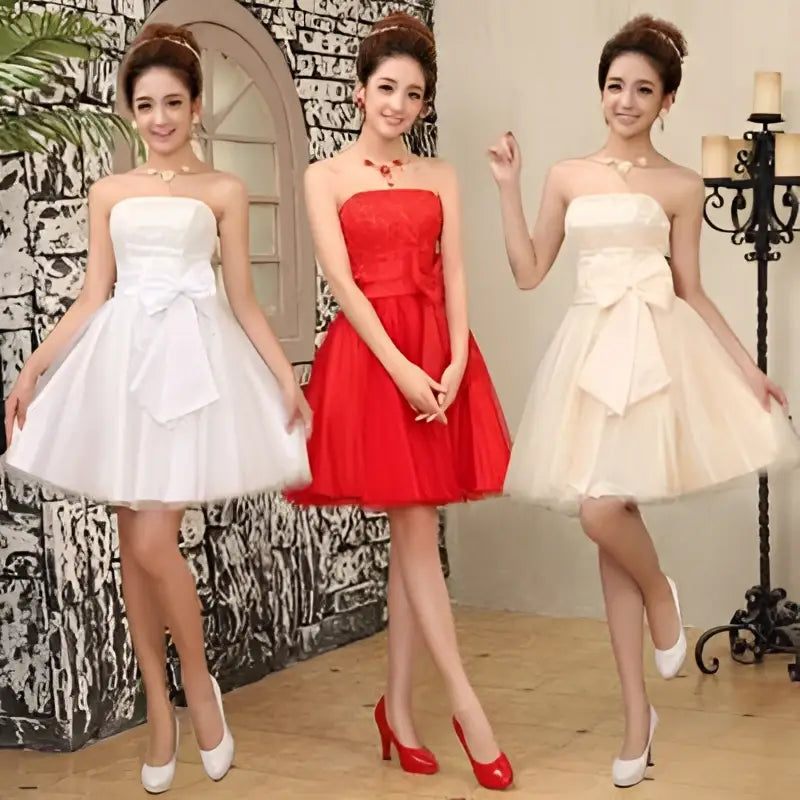Three women model strapless cream-colored tulle mini dresses with fitted bodice and large bow at the waist for weddings