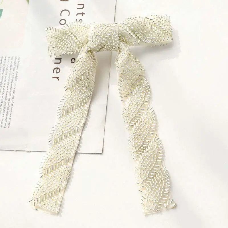 An elegant silver beaded bow hair clip with ivory texture and shimmering glass diamond accents