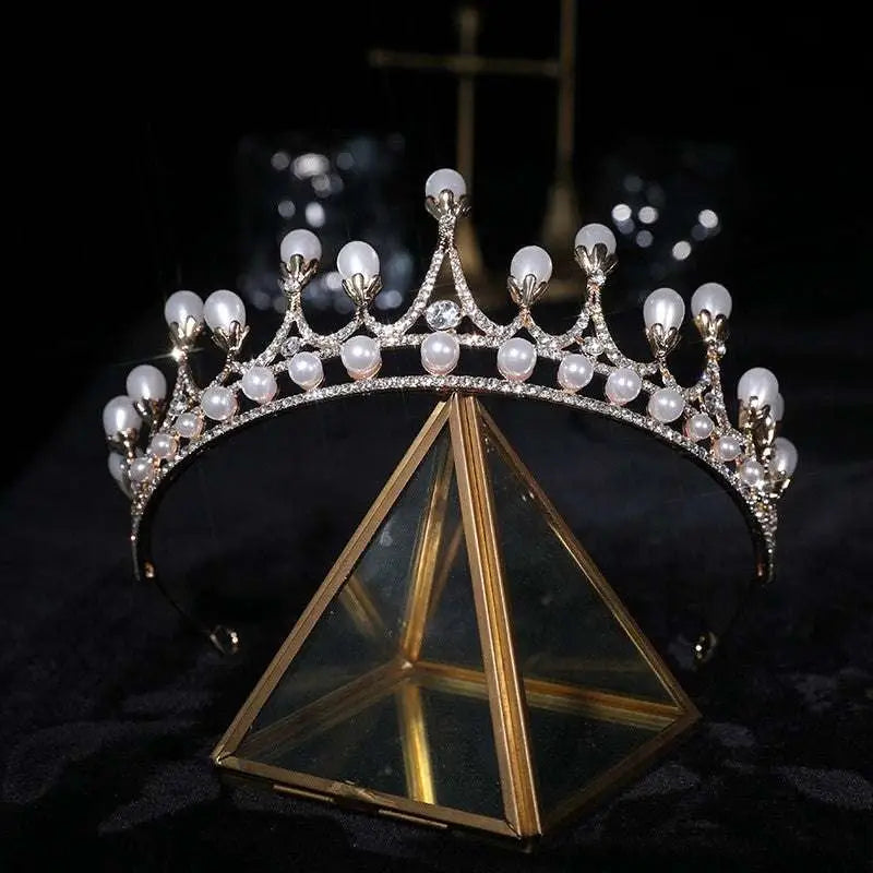Silver crown rhinestone delicate tiara with white pearls and diamonds displayed on a gold-framed glass stand