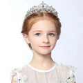 A silver crystal stage flower girl head tiara with intricate filigree and crystals worn by a young girl