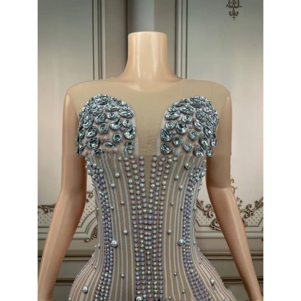 A sleeveless long gown in silver with intricate beadwork and a voluminous white feathered hips nightclub train