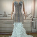 A sleeveless long gown in silver with intricate beadwork and a voluminous white feathered hips nightclub train