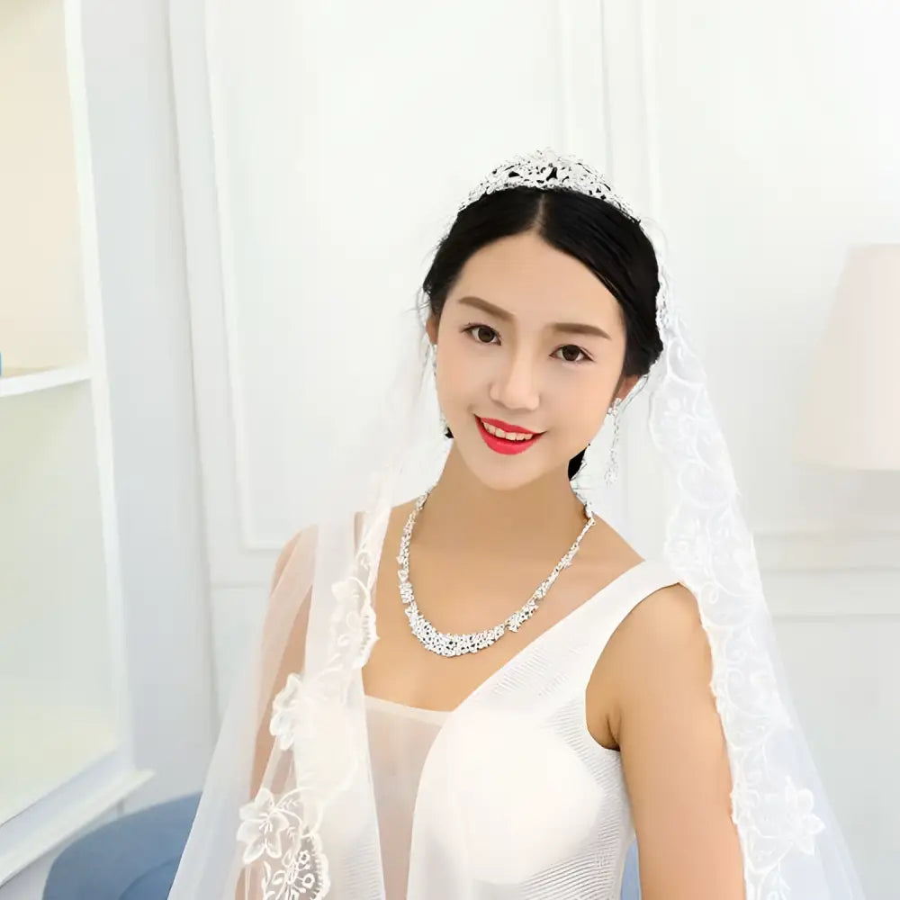 A delicate silver tiara with sparkling crystals and lace detail complements a silver floral jewelry necklace earrings set