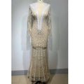 A shimmering champagne-colored backless tight fishtail gown with intricate white lace and sheer long sleeves on a mannequin