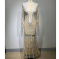 A shimmering champagne-colored backless tight fishtail gown with intricate white lace and long sheer sleeves on a mannequin