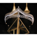 A silver bridal crown baroque adorned with baroque pearls and diamonds displayed on a gold-trimmed glass stand