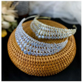 Two silver super flash zircon crown tiaras with intricate diamond-like embellishments displayed on a woven wicker base