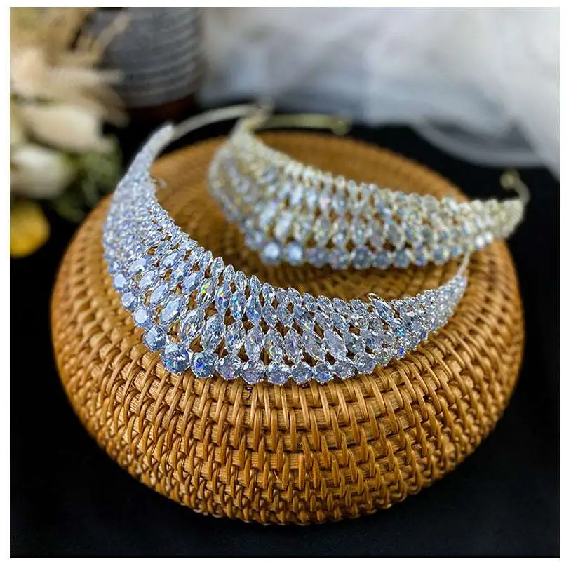 Two silver super flash zircon crown tiaras with intricate diamond-like embellishments displayed on a woven wicker base