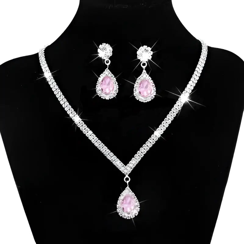 Silver v-shaped crystal bridal jewelry set featuring a sparkling silver necklace with pink teardrop pendant and matching earrings