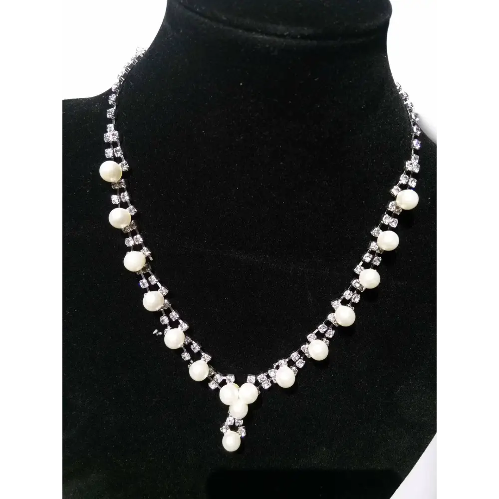 A delicate silver simple bride jewelry necklace with white pearls and rhinestones displayed on black velvet bust