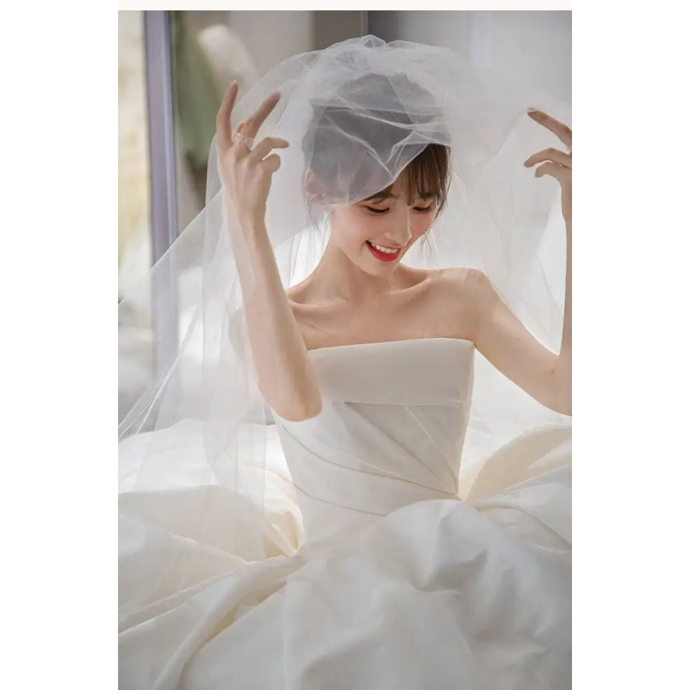 A simple elegant french style satin wedding dress paired with a flowing white satin wedding veil draping gracefully