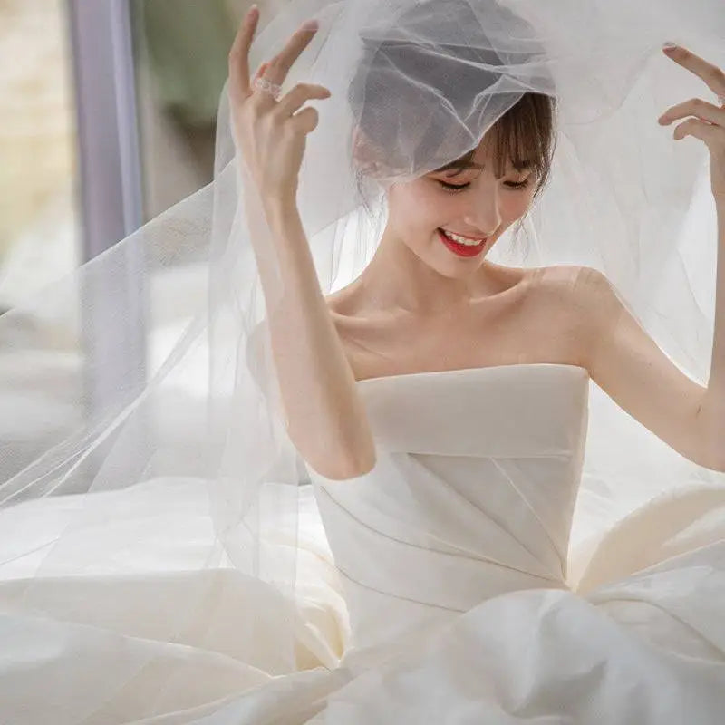 A flowing white satin wedding dress with a simple elegant french style veil draping gracefully over the bride