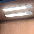Two sleek white slim motion sensor led cabinet lighting strips mounted under wooden cabinetry for modern use