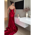 A striking crimson satin mermaid evening dress with a fitted bodice and dramatic train strapless evening dress