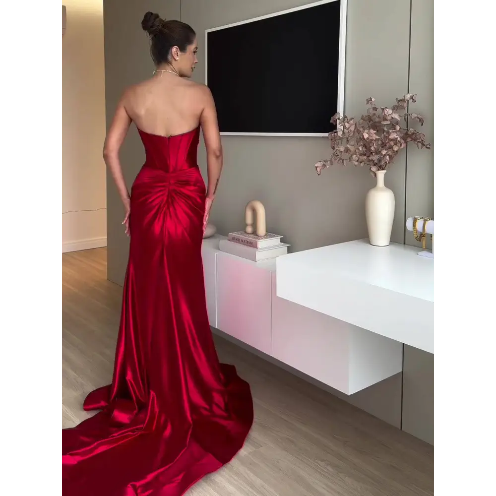 A striking crimson satin mermaid evening dress with a fitted bodice and dramatic train strapless evening dress