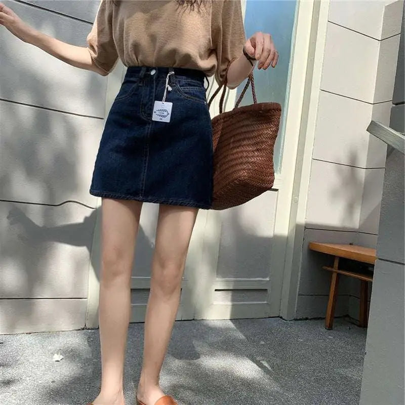 Small denim skirt in summer dark blue denim with front pocket and belt loop detail paired with straw tote bag