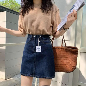 Dark blue small denim skirt with high waist and front pockets paired with a straw tote bag for summer dark blue wear