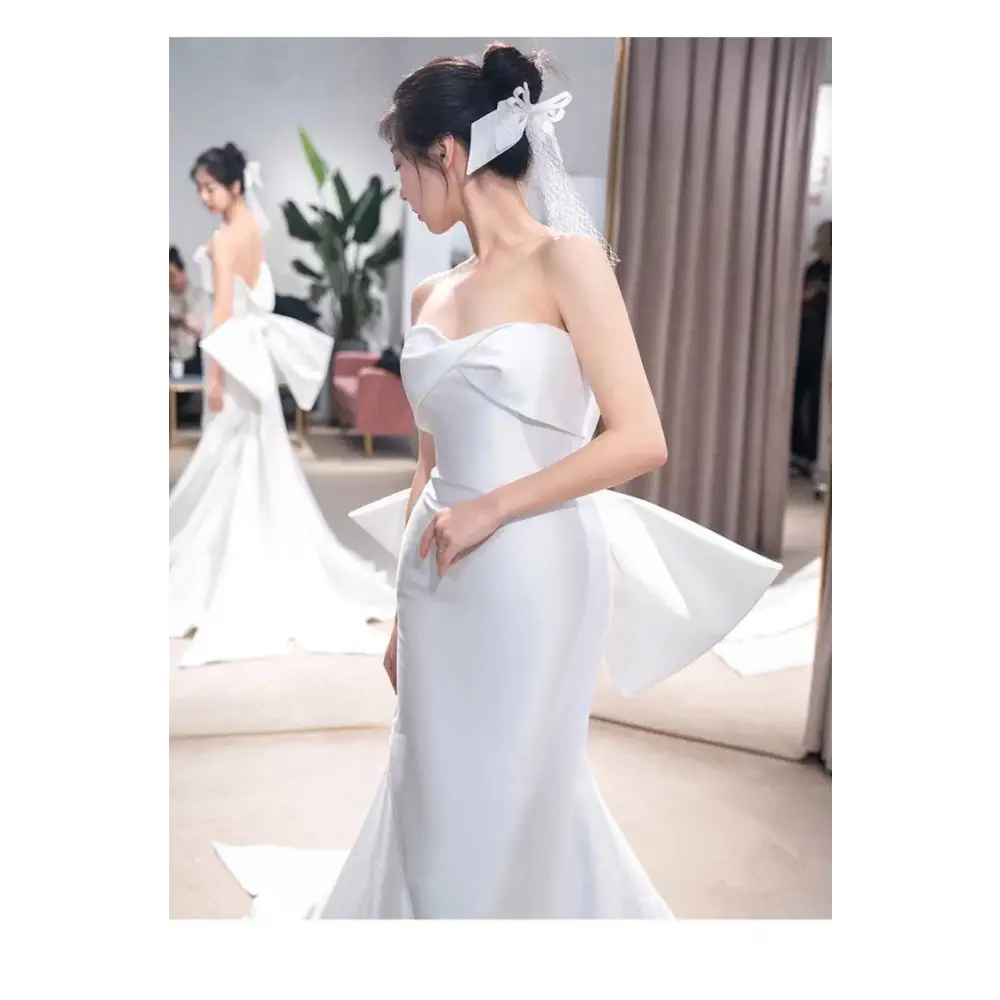 Back view of sleek white satin mermaid wedding dress with dramatic bow and small trailing temperament veil
