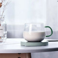Clear glass mug with green handle filled with milk on a light mint smart coffee mug warmer with three temperature settings