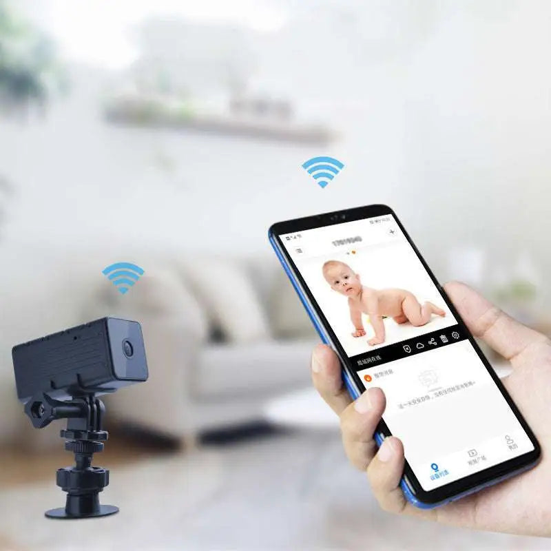 Black rectangular smart intercom network camera on stand showing live baby crawling feed on smartphone screen
