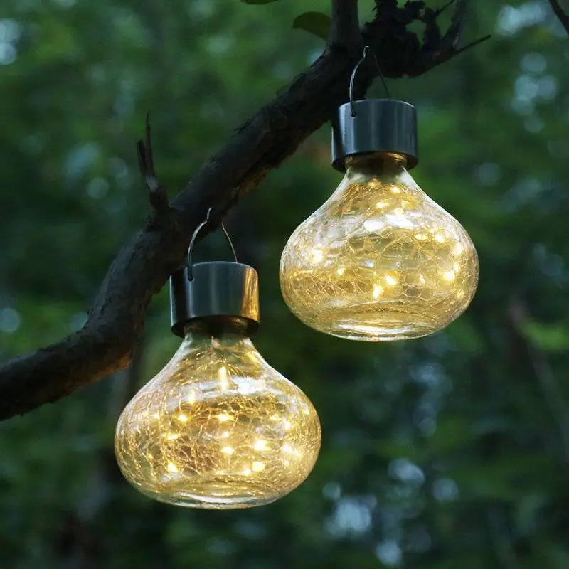 Two golden solar crackle glass small night lights with metallic caps hanging from a tree branch creating ambient light