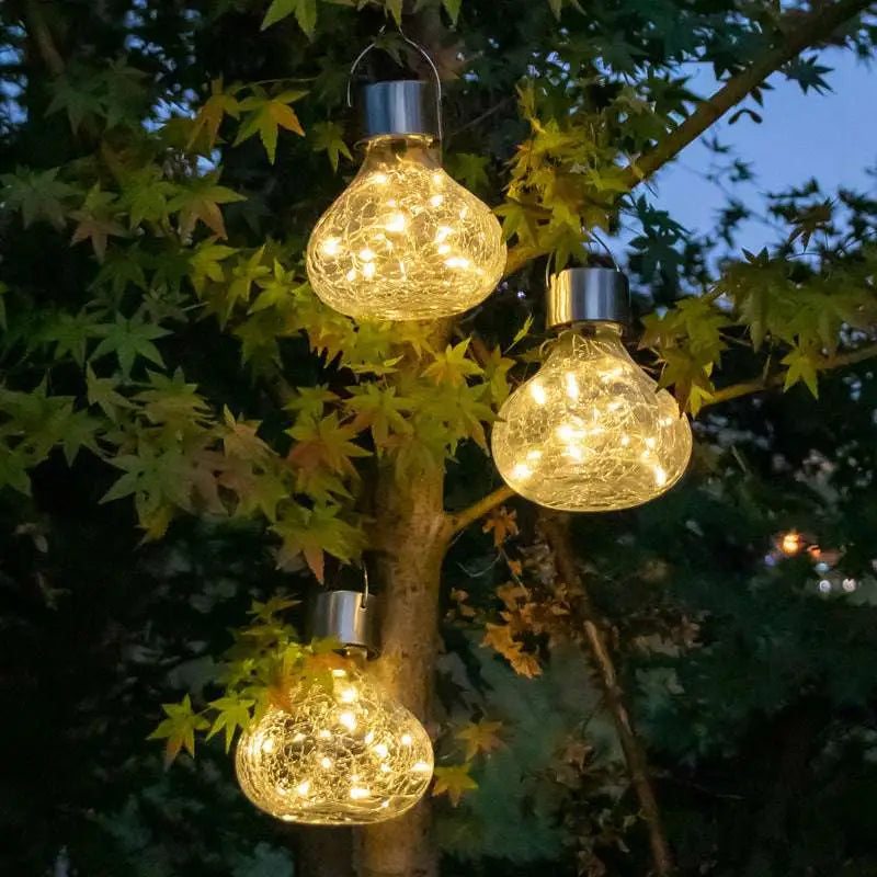 Three glowing bulb-shaped solar crackle glass small night lights with metallic tops hanging as ambient light