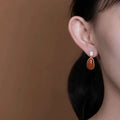 Gold-toned southern red agate lucky bean drop earrings with polished oval carnelian stone below crystal square setting