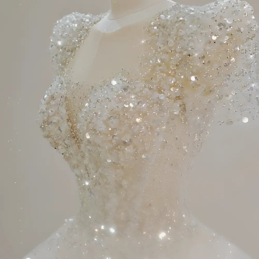 A sparkling beaded white wedding dress with intricate silver beadwork, puffed sleeves, and a voluminous white trailing wedding gown