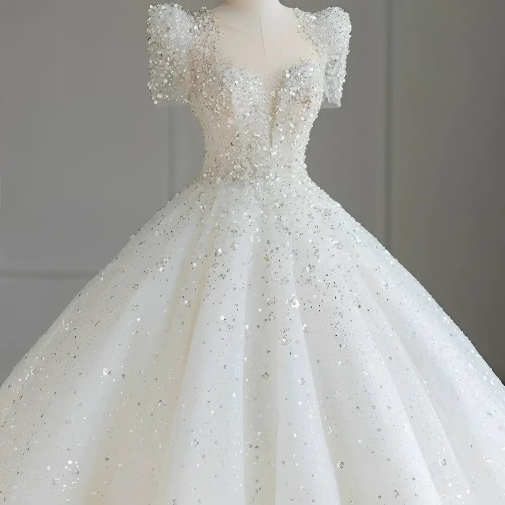 A sparkling beaded white wedding dress with short puffed sleeves and a voluminous skirt featuring intricate beading