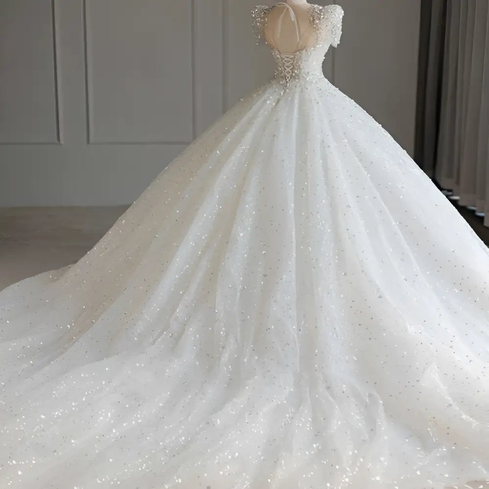 A sparkling beaded white wedding dress with off-the-shoulder sleeves and a voluminous white trailing skirt