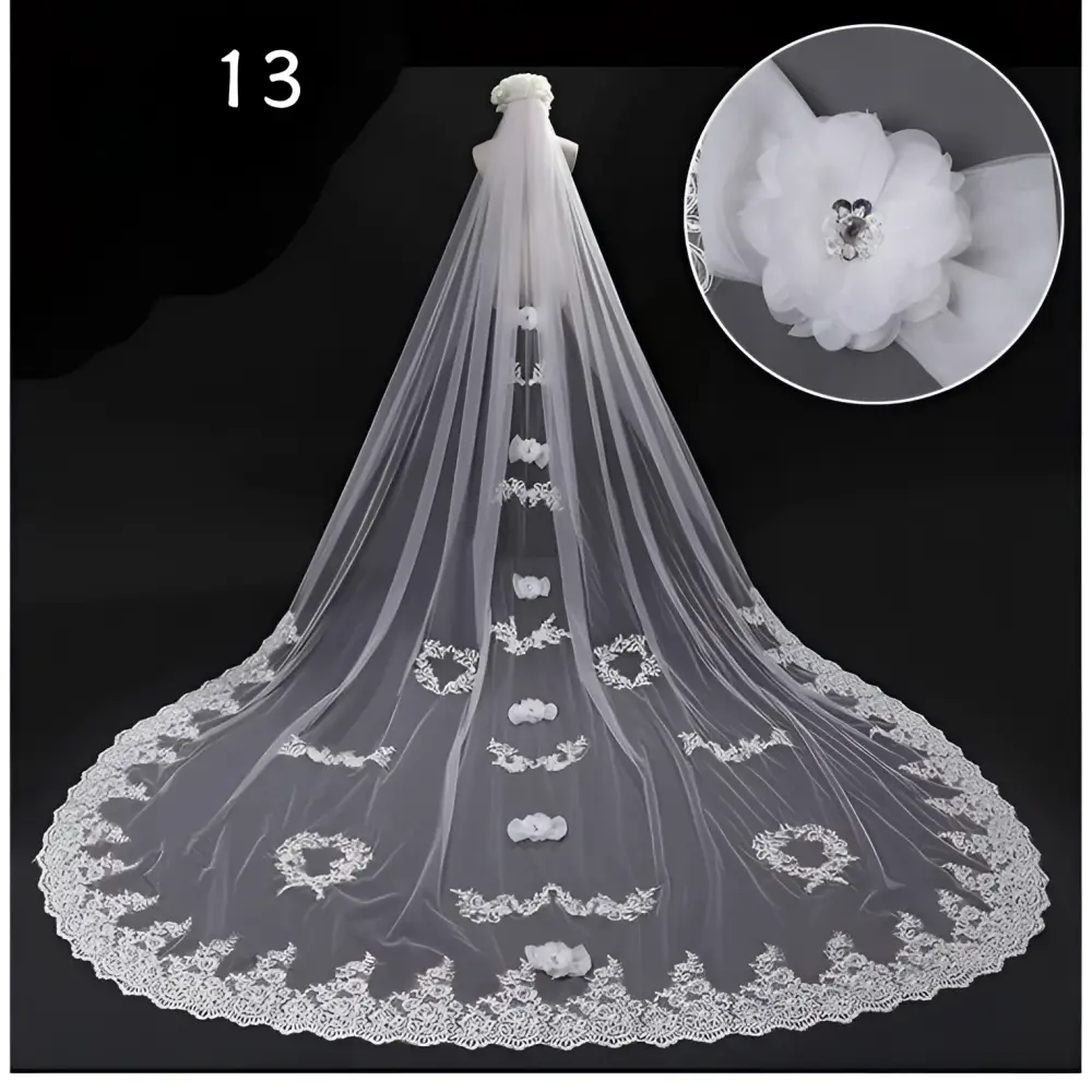 A long flowing white lace wedding dress veil with intricate floral appliqués and a decorative flower embellishment