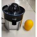 Black and silver steel electric lemon juicer with transparent dome for efficient lemon juicing next to a bright yellow orange