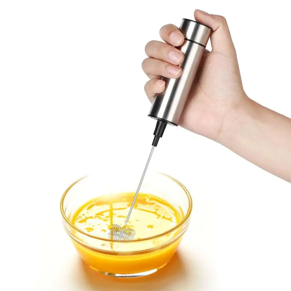 Silver stainless steel milk frother and coffee stirrer with slender shaft and mesh whisk tip whipping liquid in glass bowl