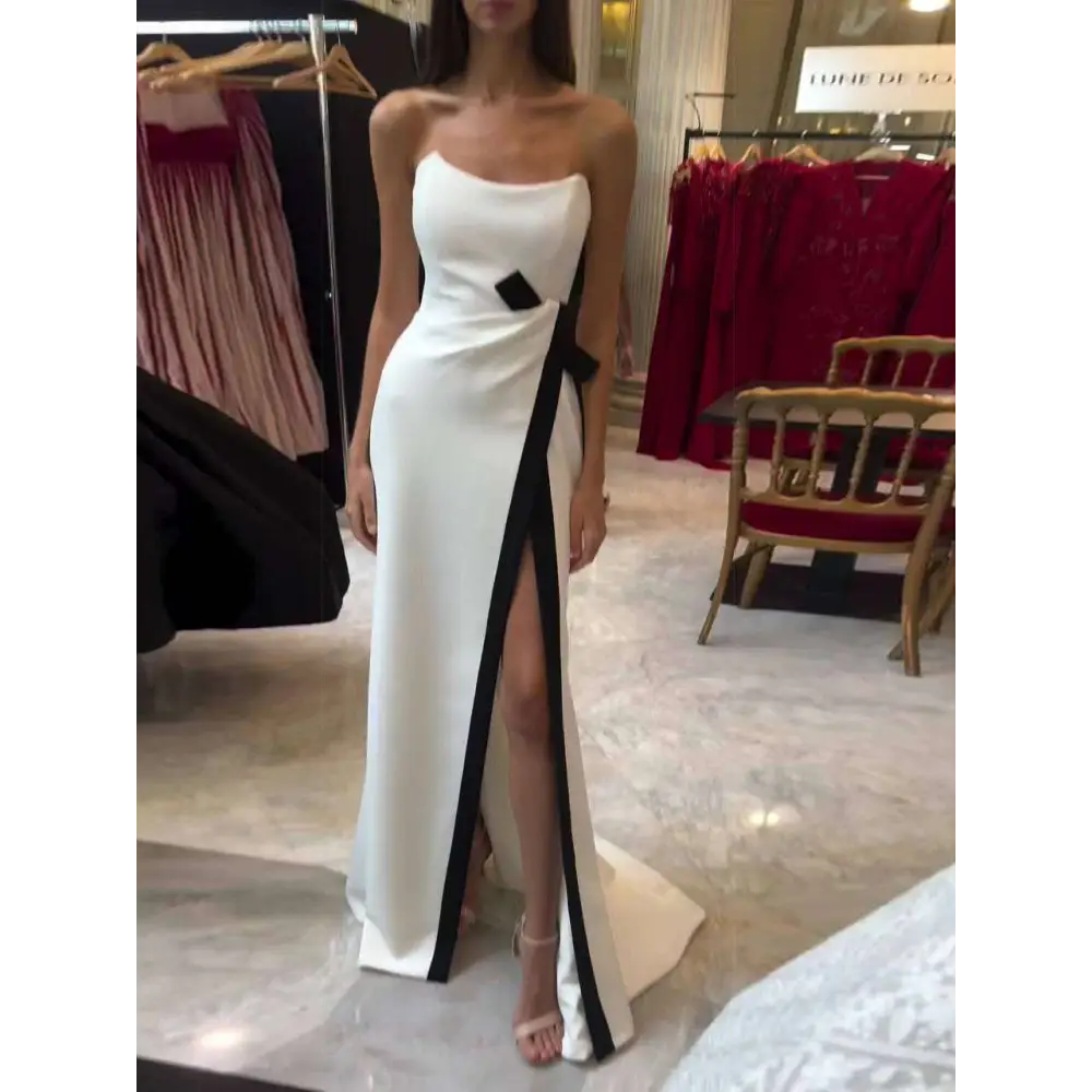 A strapless black and white contrasting slit dress in sleek white satin with a bold black diagonal stripe and bow accent
