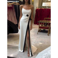 A strapless black and white contrasting slit dress in sleek white satin with a bold black diagonal stripe and bow accent