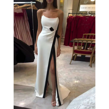 A strapless black and white contrasting slit dress in sleek white satin with a bold black diagonal stripe and bow accent