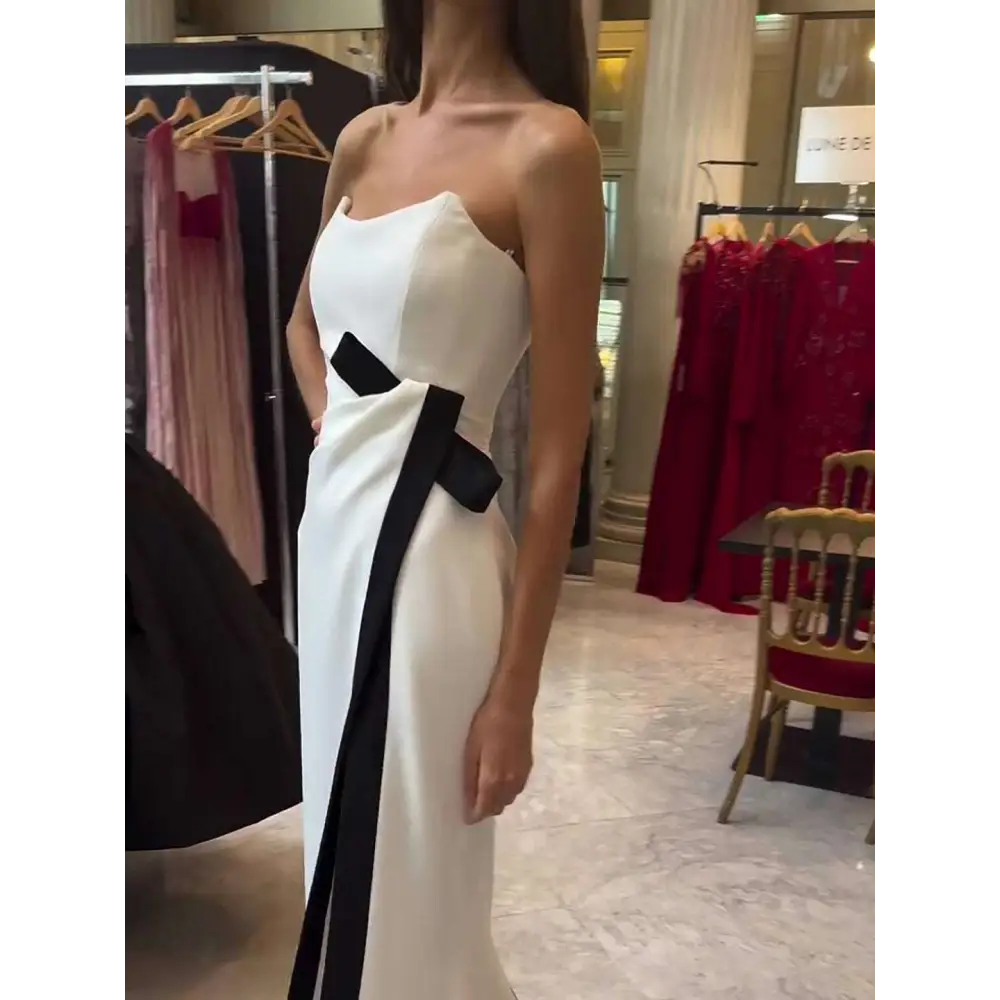 A strapless black and white contrasting slit dress in sleek white satin with a bold black diagonal stripe and bow accent